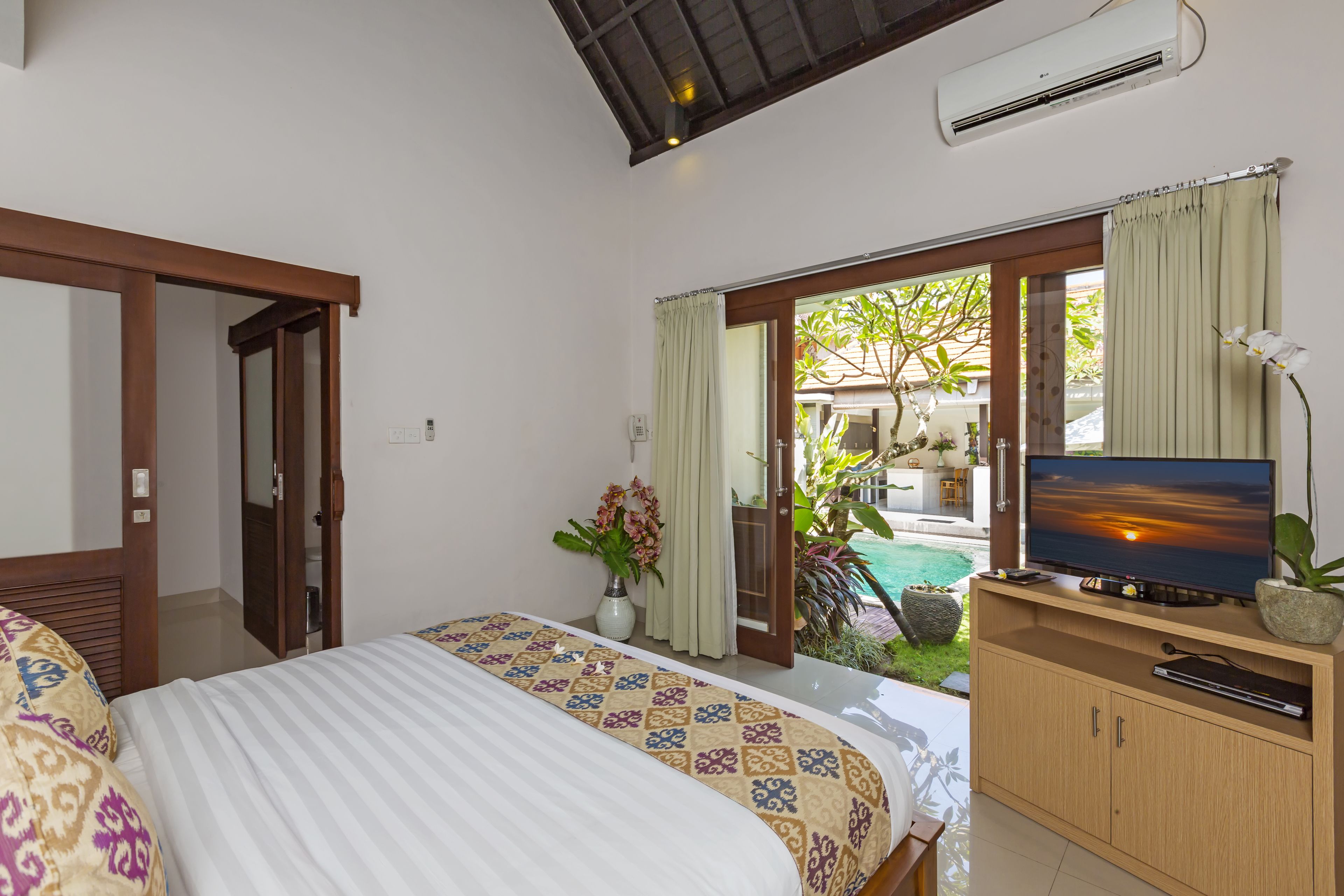 A bedroom with a bed, a TV, and a view of a pool.