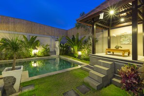 A swimming pool with surrounding greenery, a wooden deck, and a bench. - Kubal Villa and Living Seminyak (Seminyak)