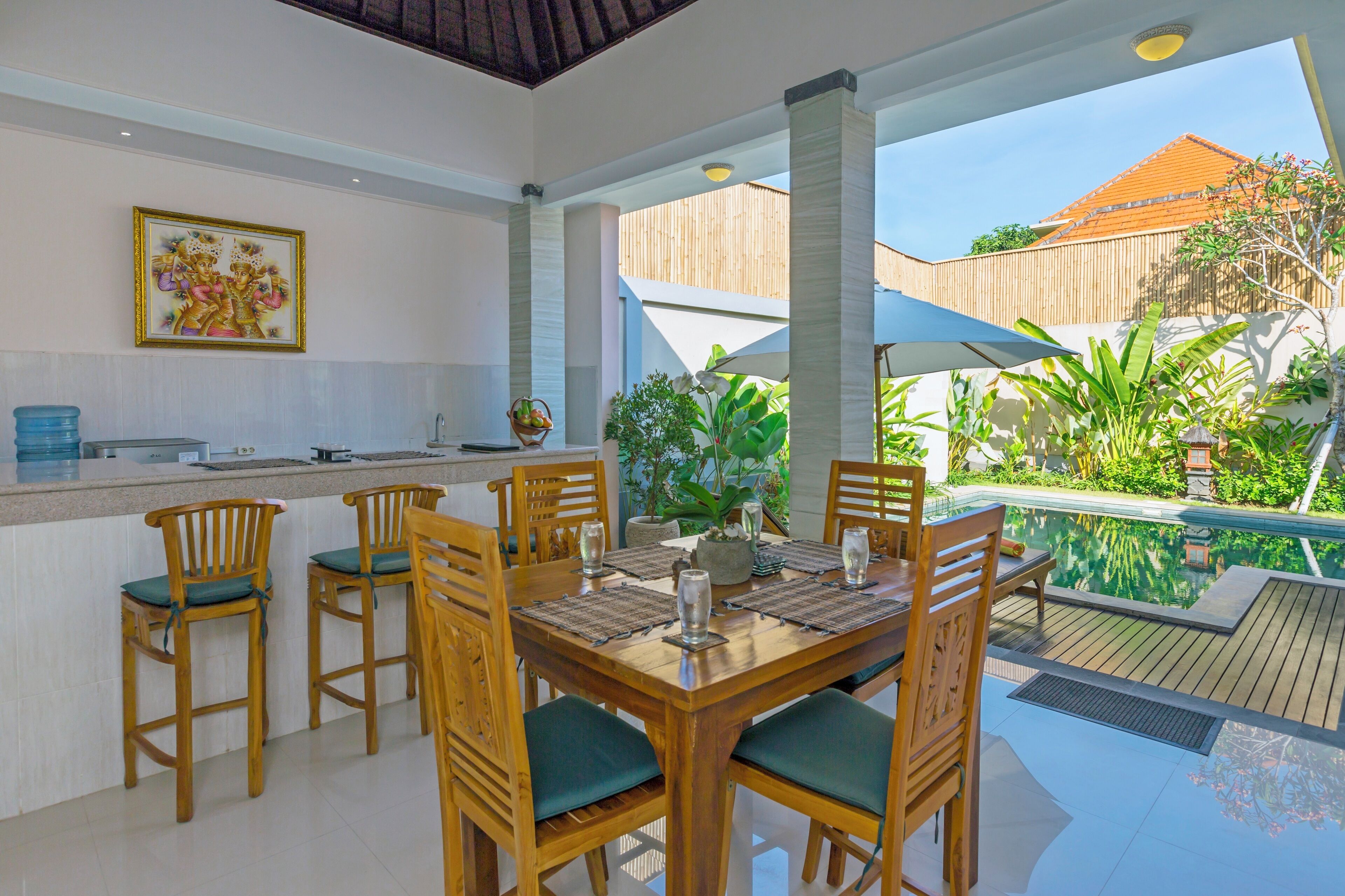 A dining area with a wooden table and chairs, a bar counter, and a view of a swimming pool.