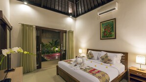 Une chambre d’hôtel avec un lit, une table de chevet, une commode, une plante en pot et une fenêtre avec des rideaux.