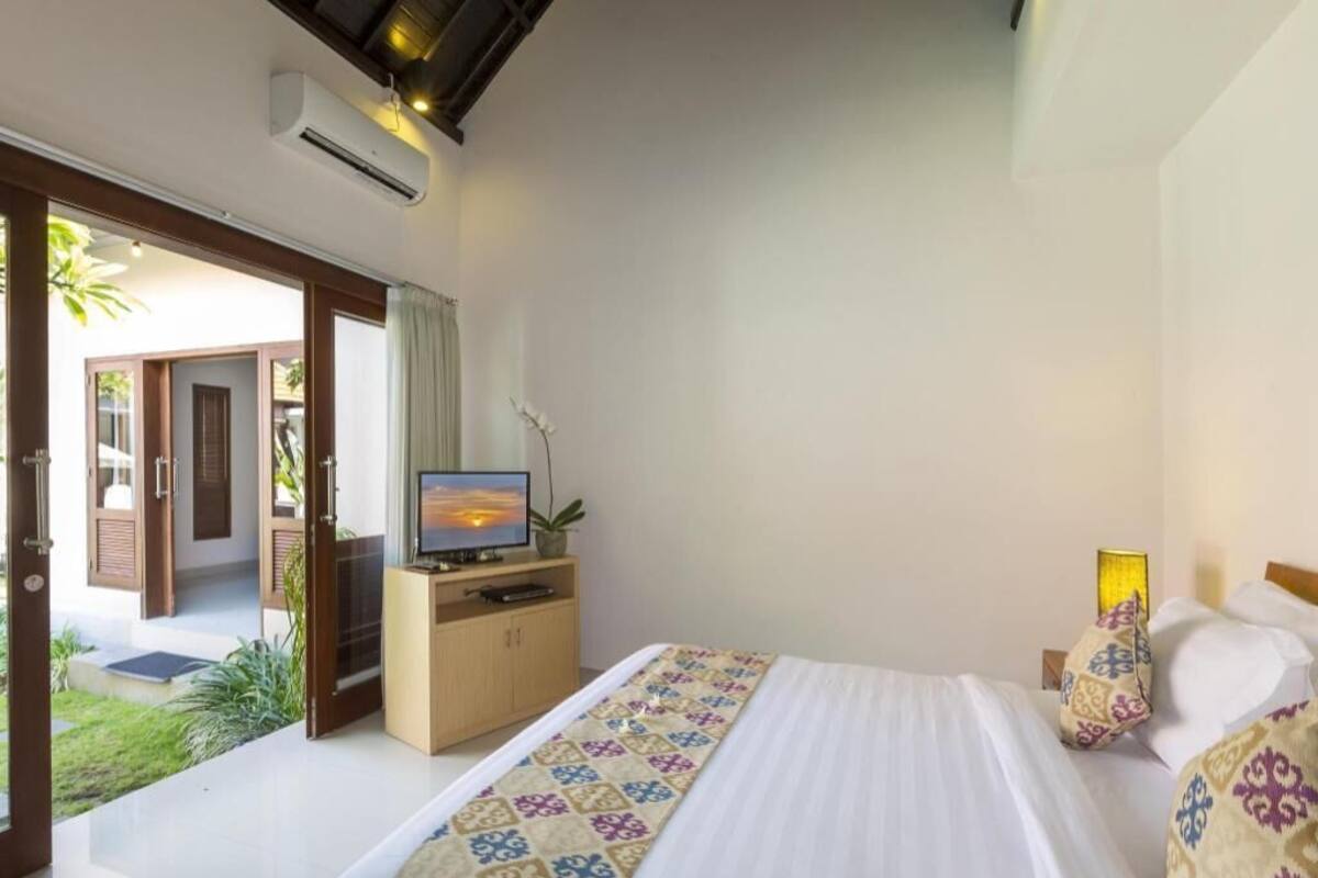 Habitación de hotel con una cama, un televisor sobre un mueble de madera, una lámpara de noche y vistas al exterior.