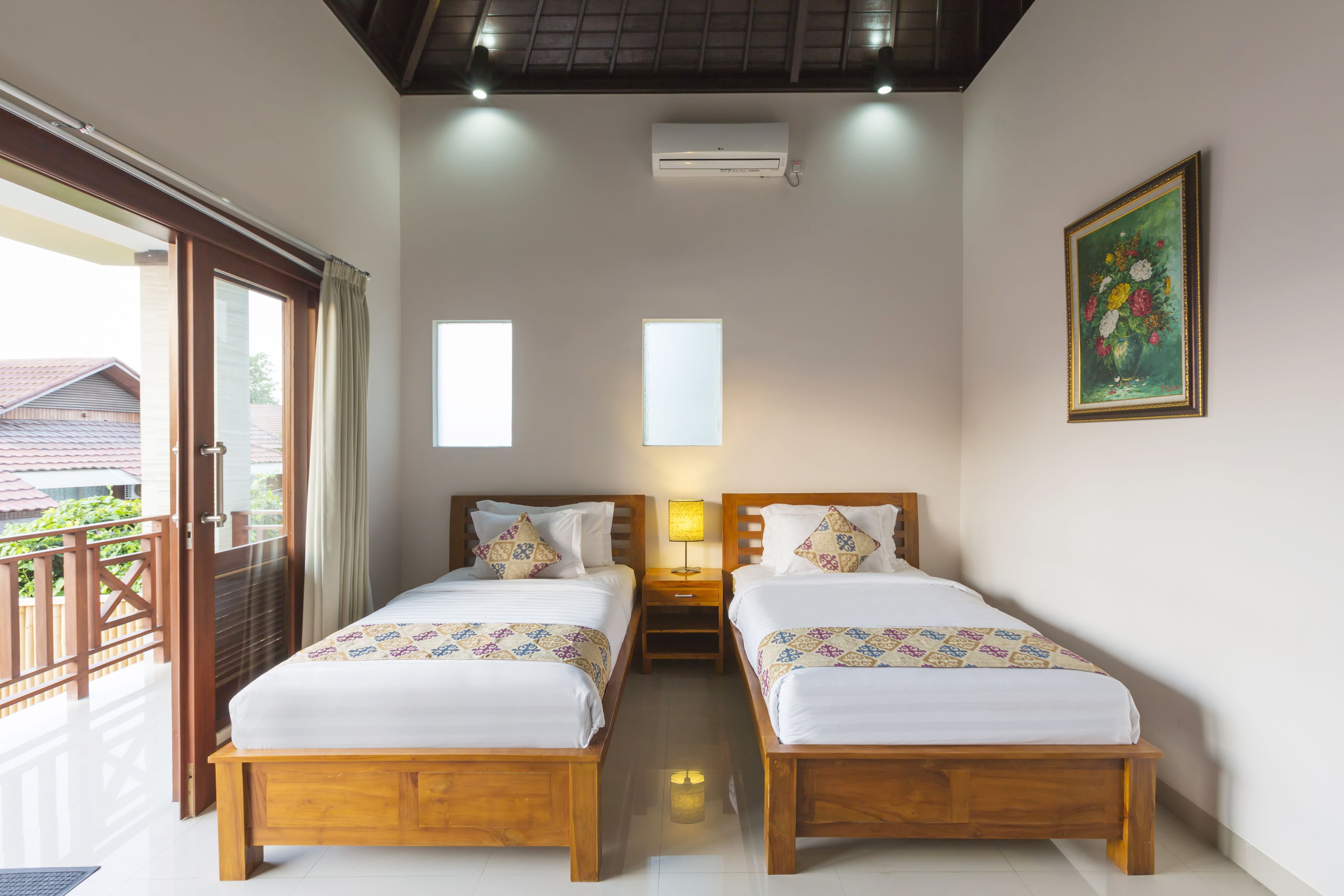 Habitación de hotel con dos camas de madera, un balcón y un cuadro en la pared.