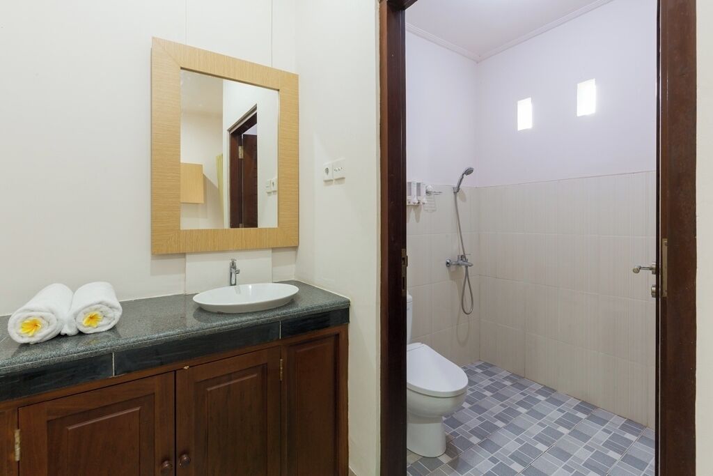 A bathroom with a wooden vanity, a sink, a mirror, and a shower area.