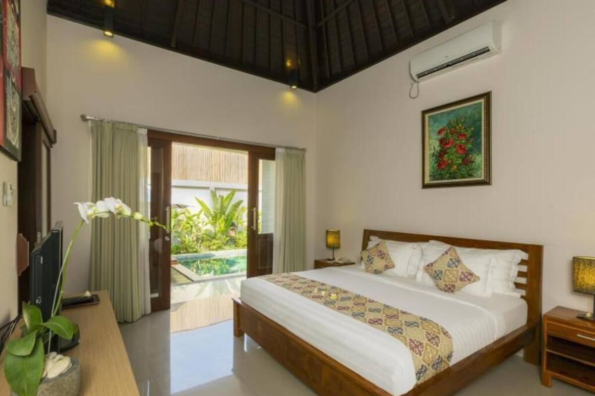 Un dormitorio con una cama grande, un escritorio, una silla, una planta en maceta y vistas al exterior.