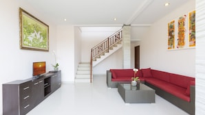 Un salon moderne avec un escalier, un canapé rouge, une table basse et un téléviseur posé sur un meuble.