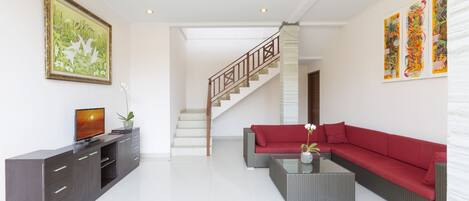 A modern living room with a staircase, a red sofa, a coffee table, and a TV on a cabinet.