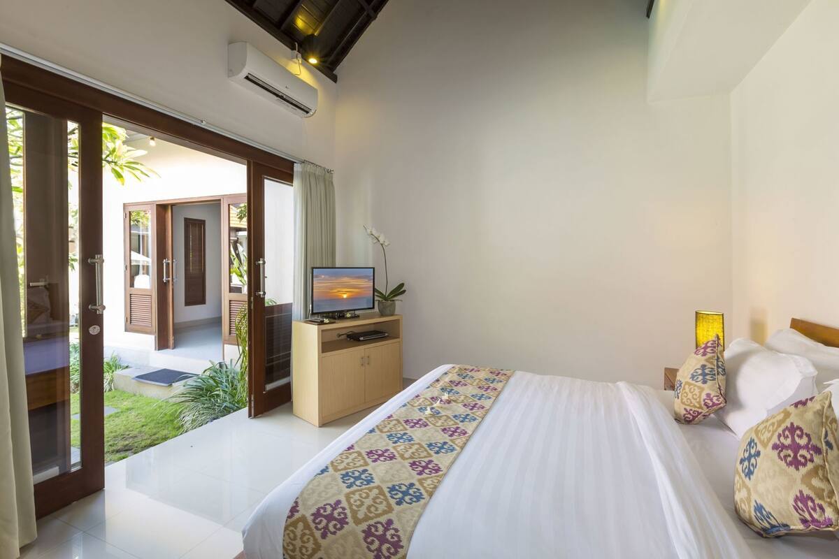 Habitación de hotel con una cama, un televisor sobre un mueble de madera y vistas al exterior.