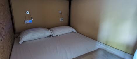 A single bed with white bedding in a room with wooden ceiling beams and beige walls.