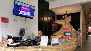 Een houten toonbank in de vorm van een boot, met een laptop, papieren en een vlag. Een televisiescherm toont huurprijzen.