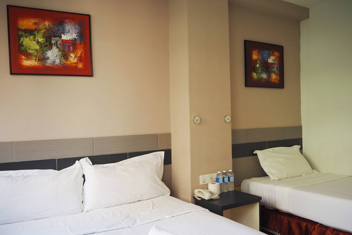 Hotelkamer met twee bedden, een nachtkastje met telefoon en waterflesjes, en twee abstracte schilderijen aan de muur.