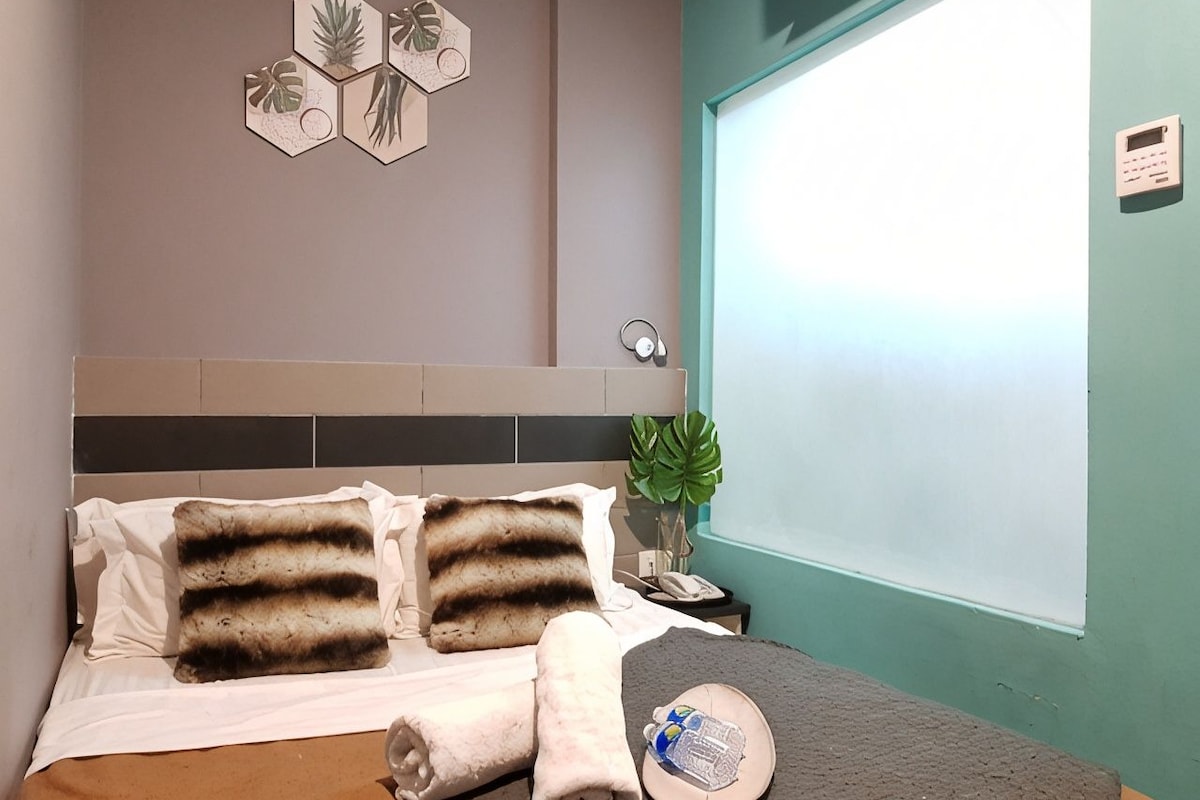 Een netjes opgemaakt bed met gestreepte kussens, een kamerplant en een aan de muur bevestigd telefoon.