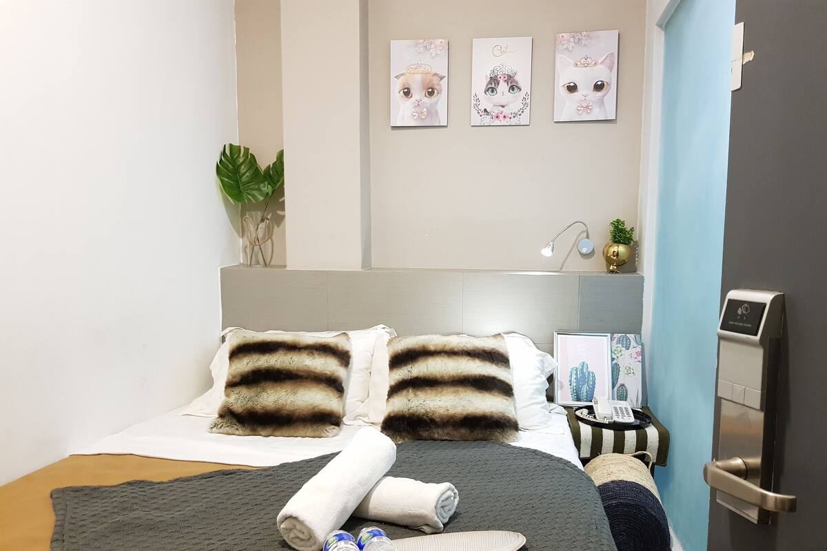 Een opgemaakt bed met gestreepte kussens, een grijze deken en een dienblad met waterflesjes.
