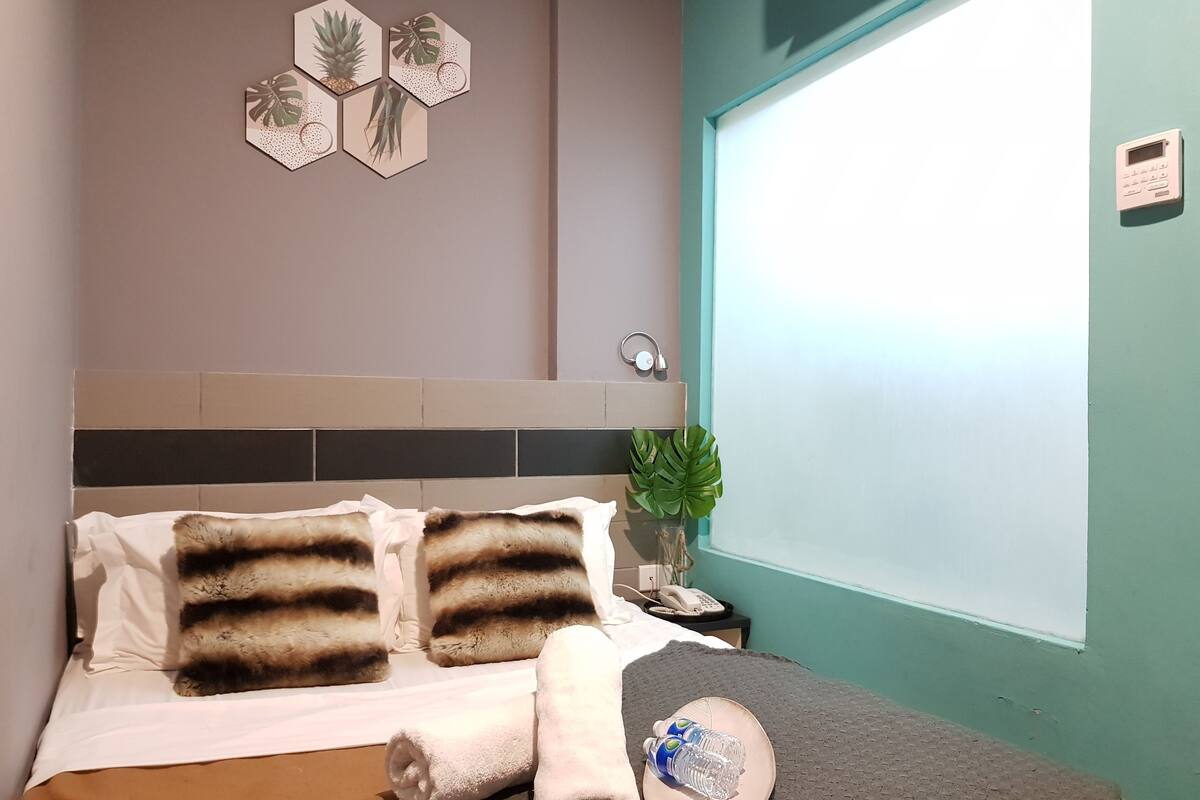 Een net opgemaakt bed met gestreepte kussens, een opgerolde handdoek en een waterfles op een dienblad.