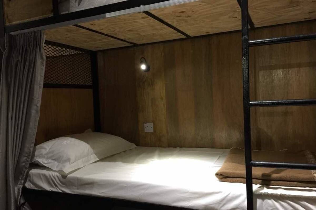 Een stapelbed met een eenpersoonsbed bovenop en een onderbed. Daarboven bevindt zich een kleine lamp, en een stopcontact op de muur.