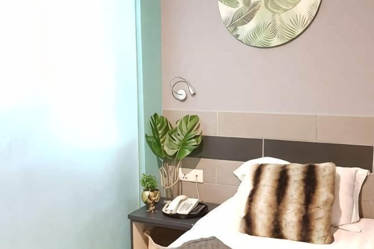 Een hotelkamer met een bed, een nachtkastje, een aan de muur bevestigd telefoon en een decoratieve plant.