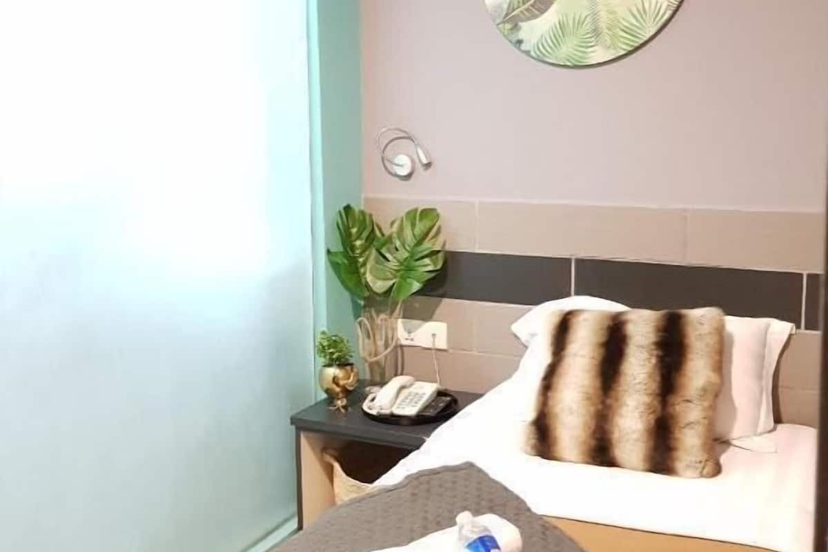 A hotel room with a bed, a bedside table with a phone, a plant, and a wall art piece.