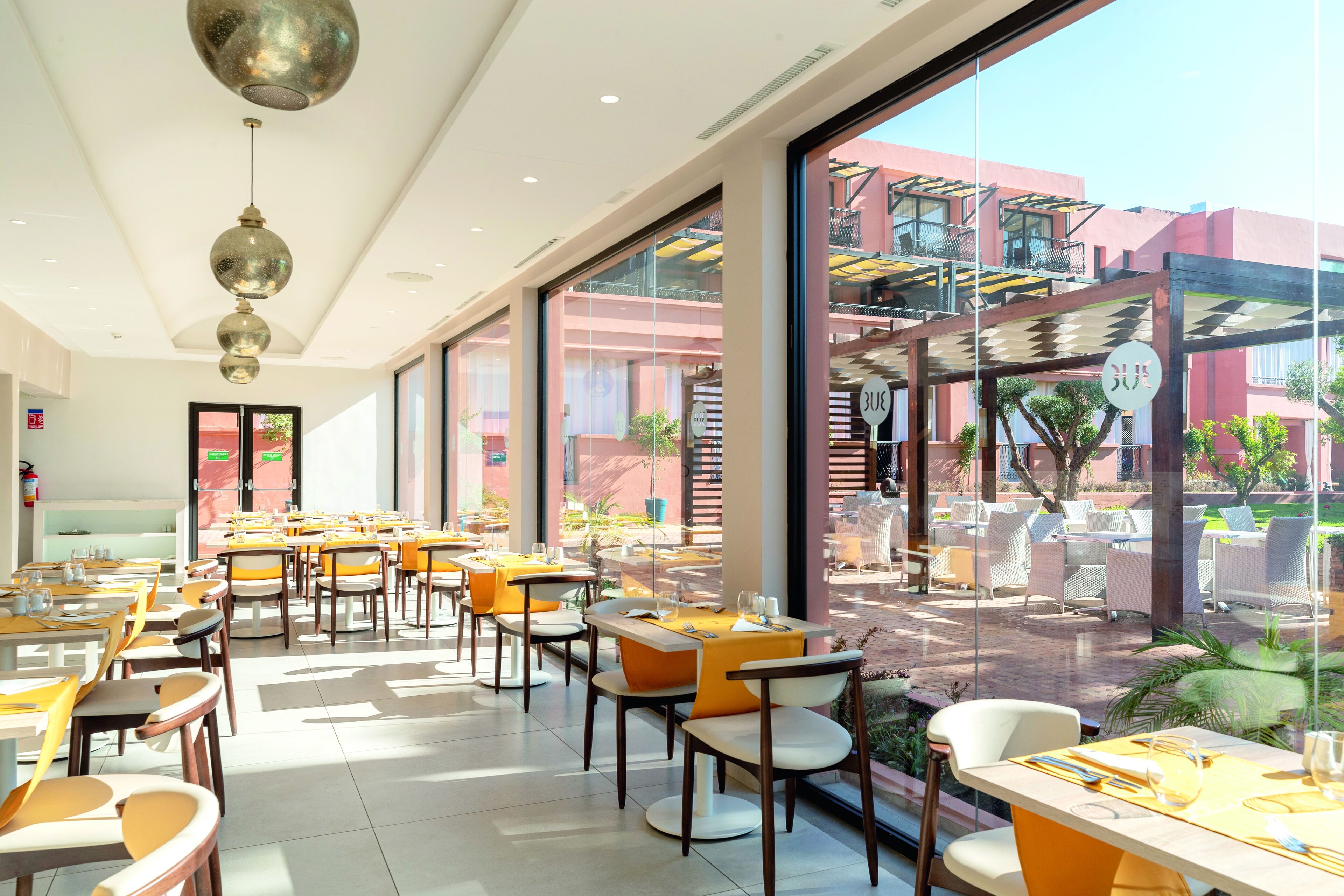 Un restaurant doté d’une salle à manger intérieure, de grandes fenêtres et offrant une vue sur la terrasse extérieure.