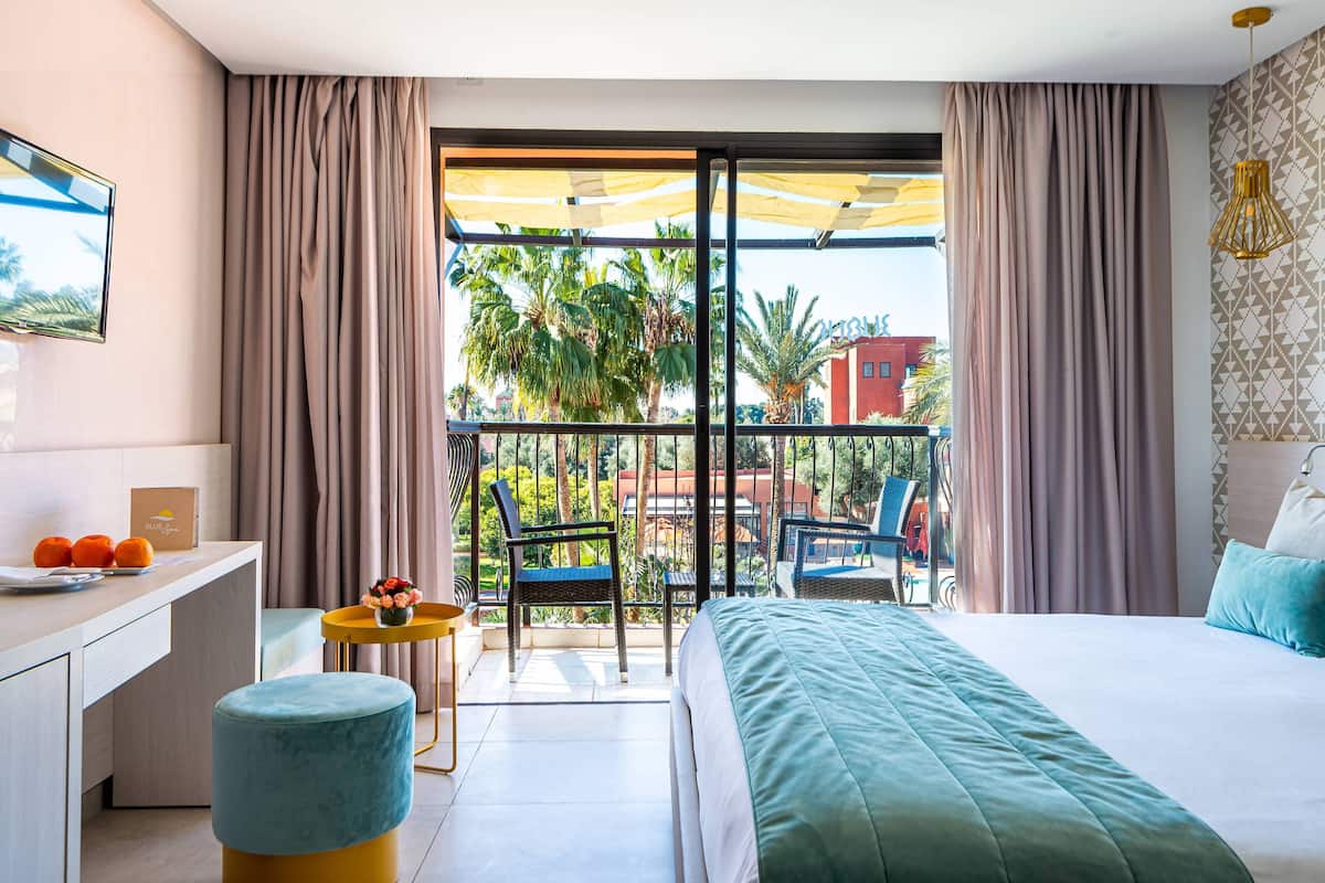 Habitación de hotel con balcón, cama, escritorio y una silla.