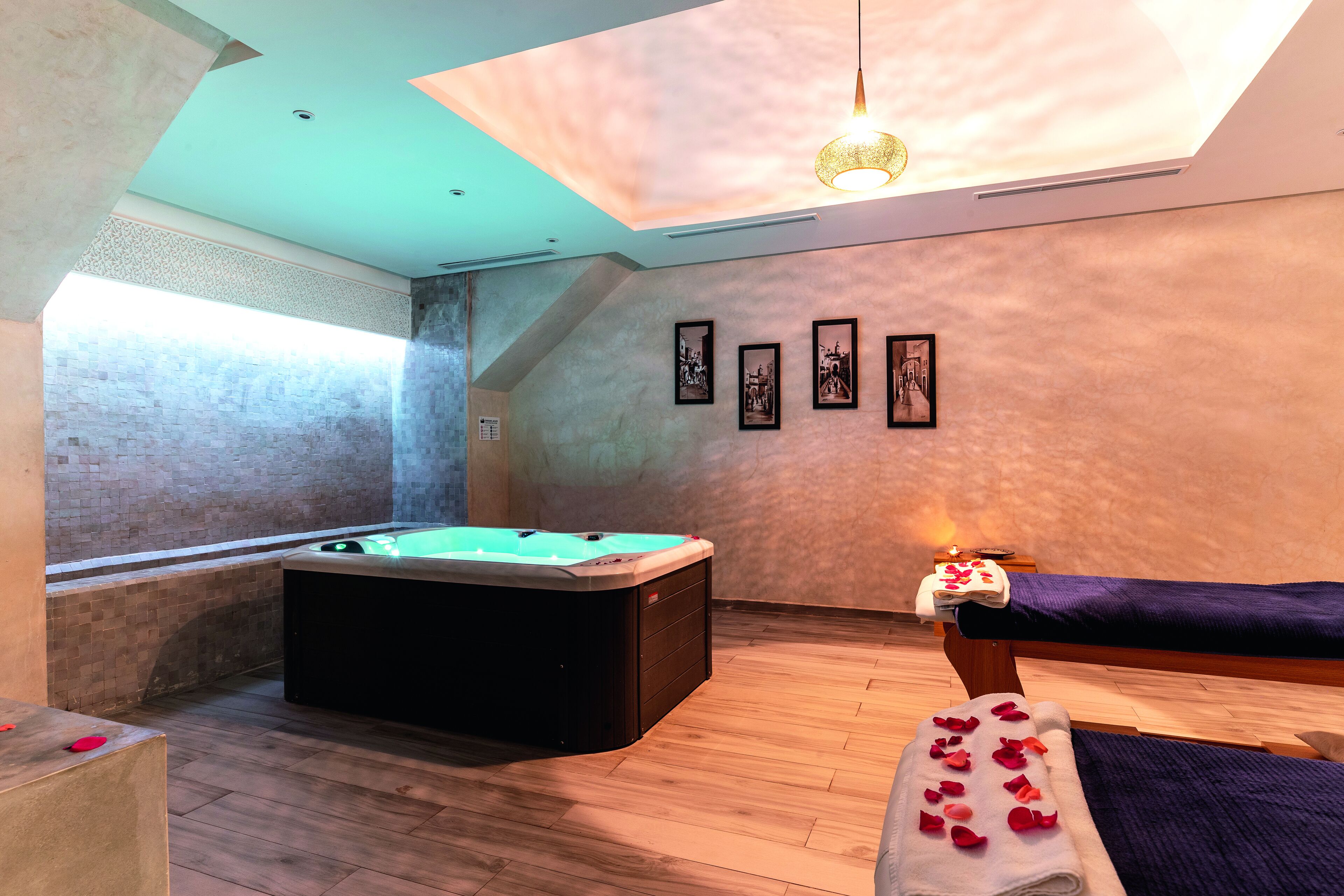 Une salle de spa équipée d’un bain à remous, d’une table de massage et de tableaux encadrés aux murs.