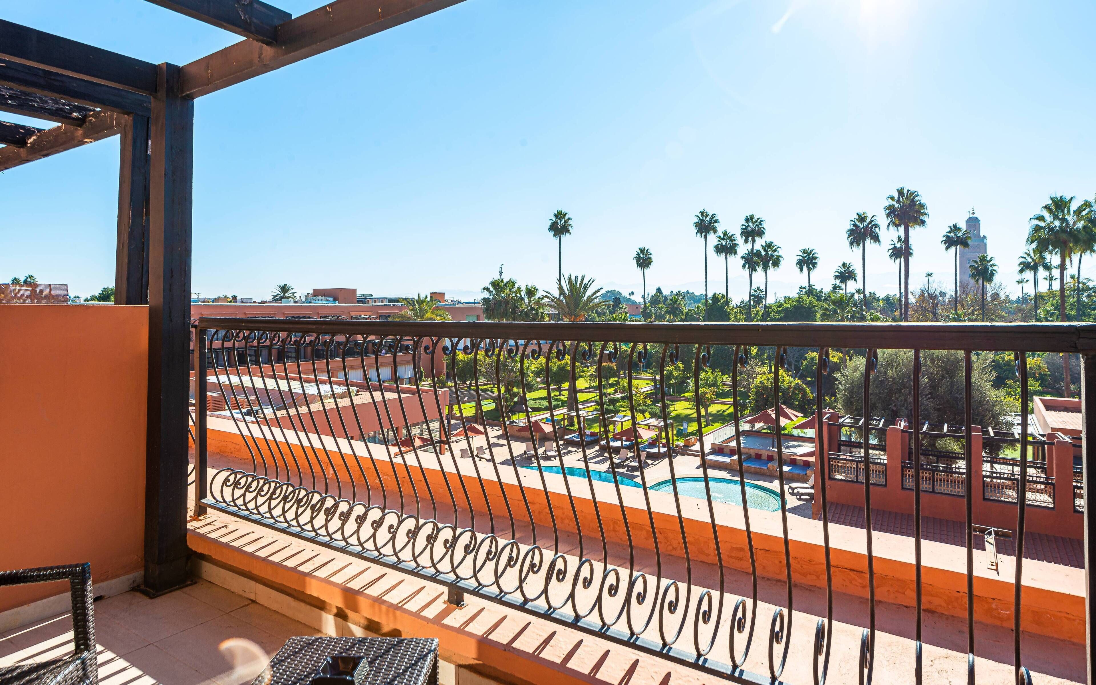 A balcony with a view of a swimming pool, palm trees, and a building in the background.