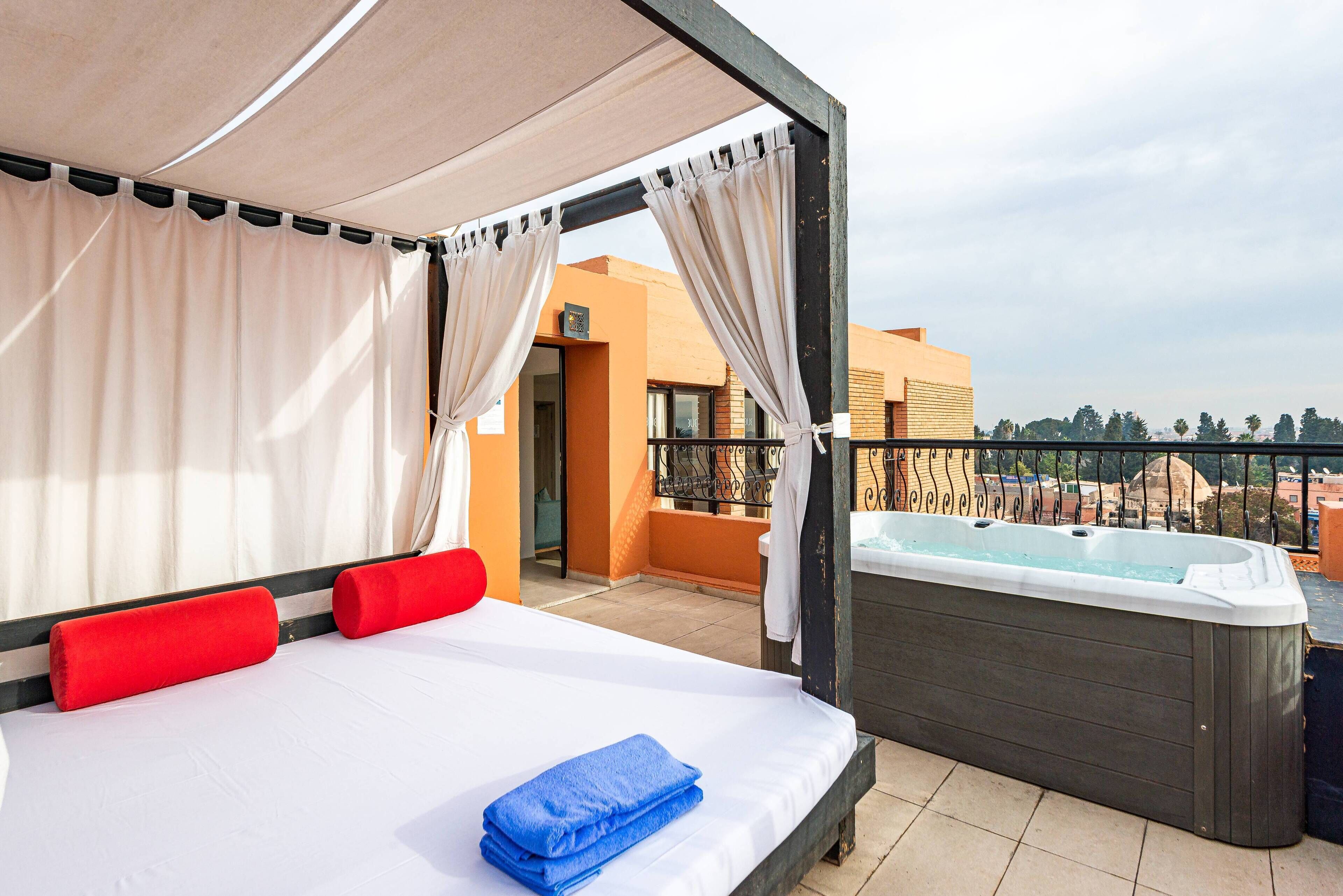 Un balcón con una cama, un jacuzzi y vistas a edificios.
