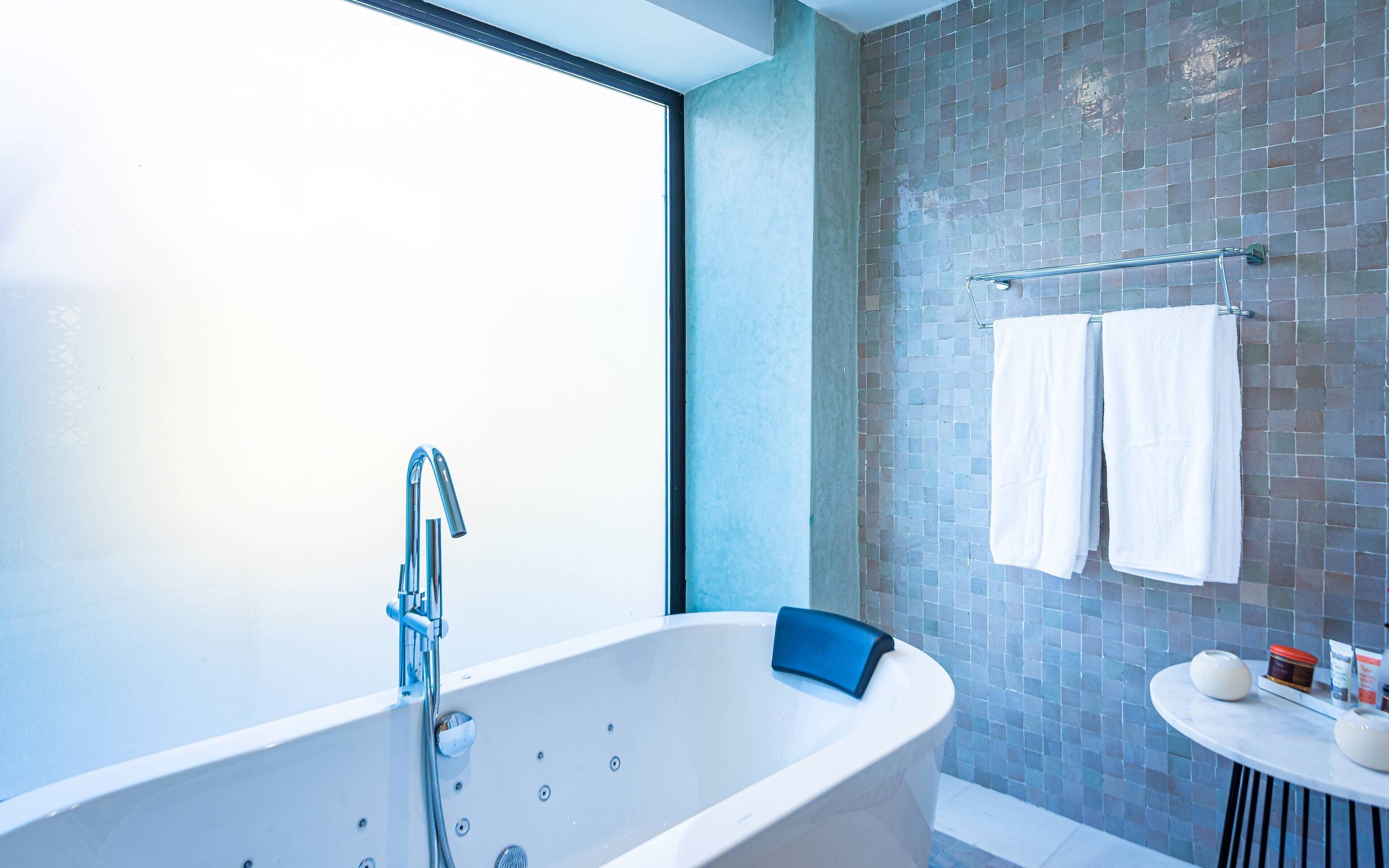 Un baño moderno con una bañera independiente, un lavabo pequeño y redondo, y un muro cubierto de azulejos.