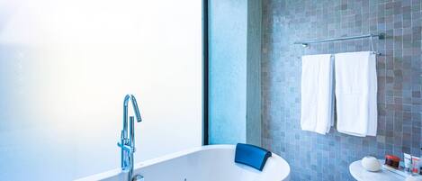 Un baño moderno con una bañera independiente, un lavabo pequeño y redondo, y un muro cubierto de azulejos.