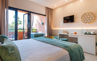 Habitación de hotel con cama, escritorio, televisión y balcón con vista a palmeras.