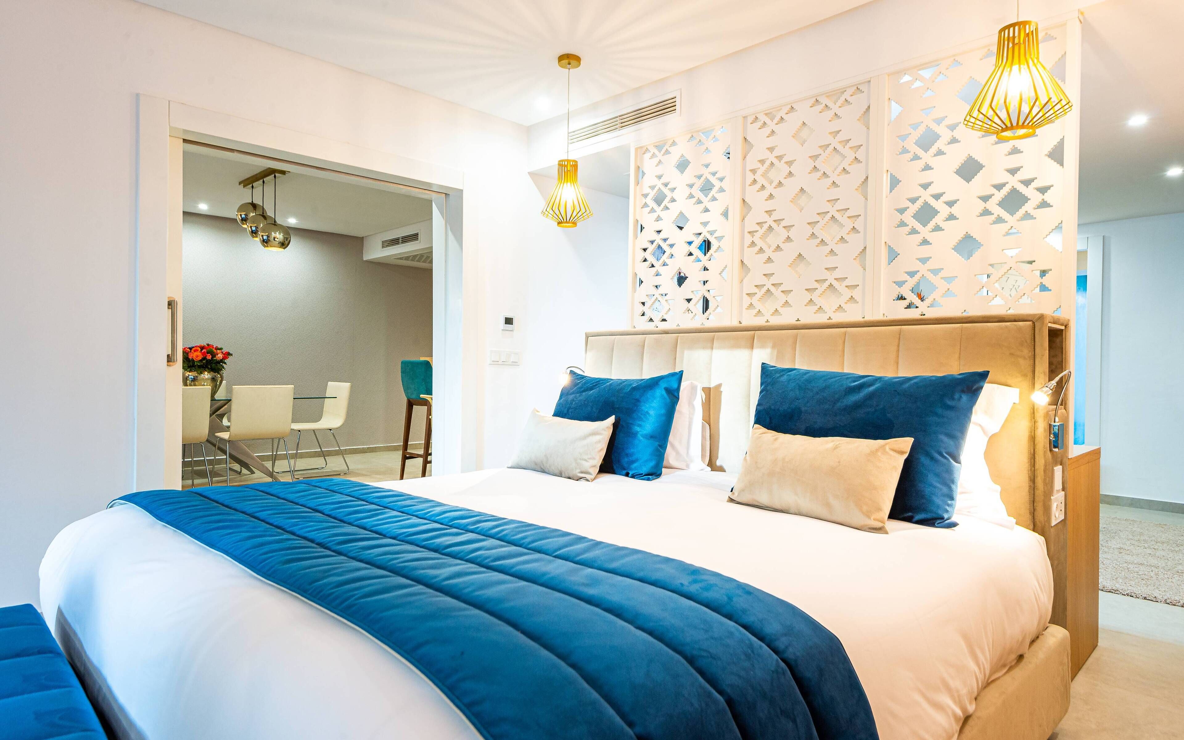 A modern bedroom with a large bed, two bedside lamps, and a decorative wall panel.