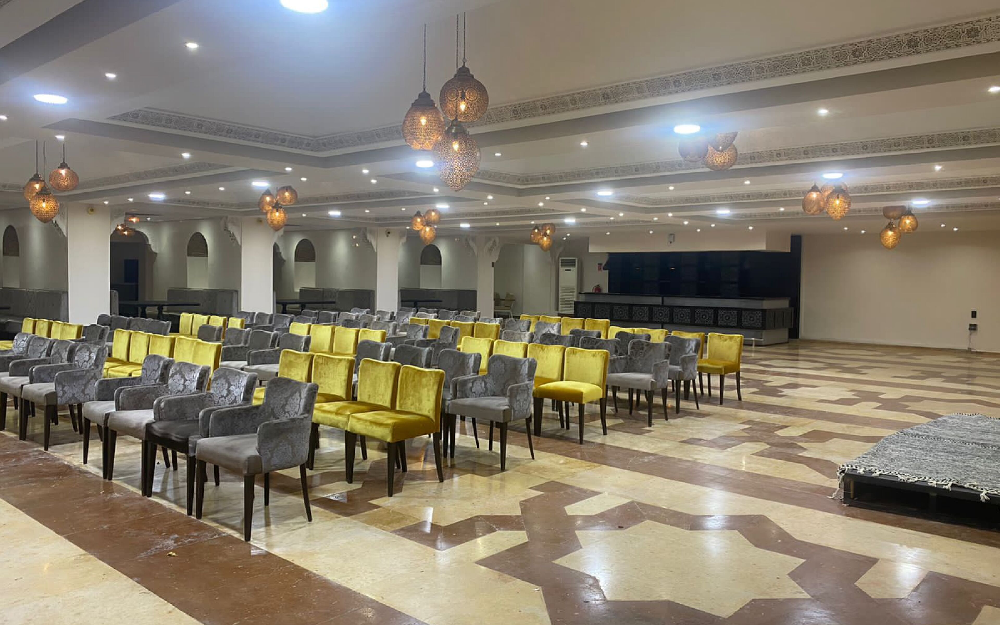 A large hall with rows of chairs, a stage, and decorative lighting.