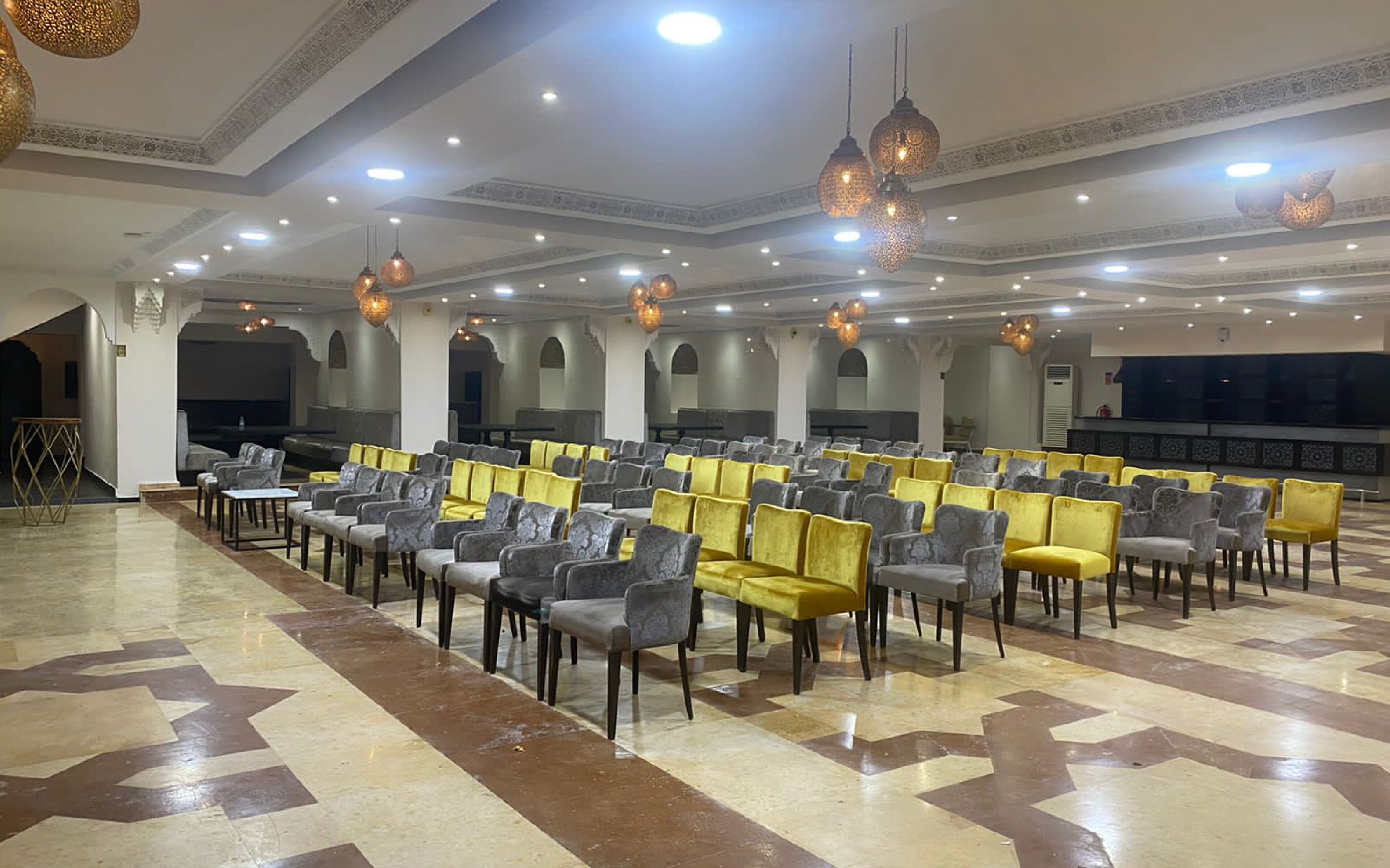 A spacious hall with rows of chairs, a patterned floor, and decorative ceiling lights.