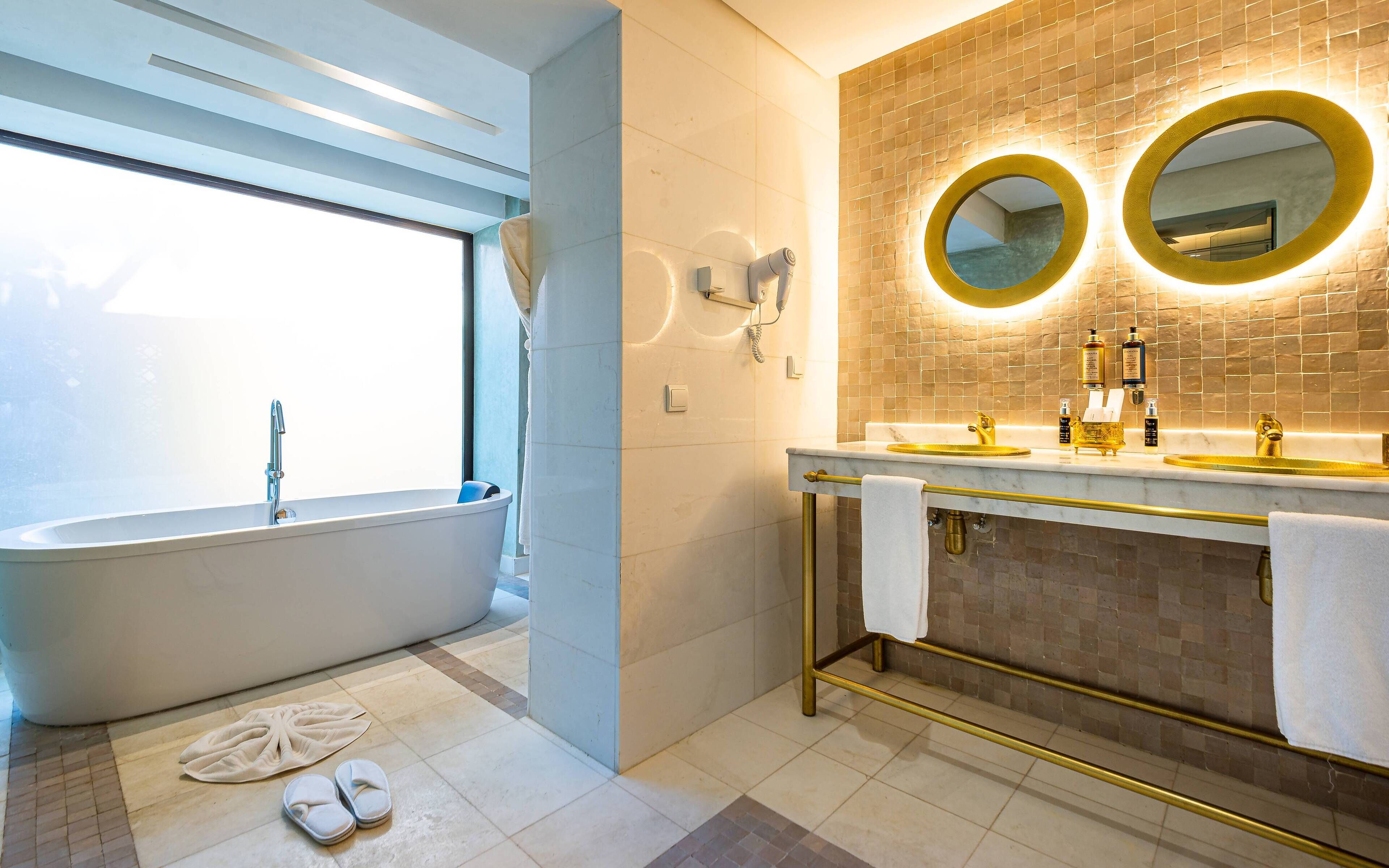 A modern bathroom with a freestanding bathtub, a vanity with dual sinks, and a large mirror with a gold frame.