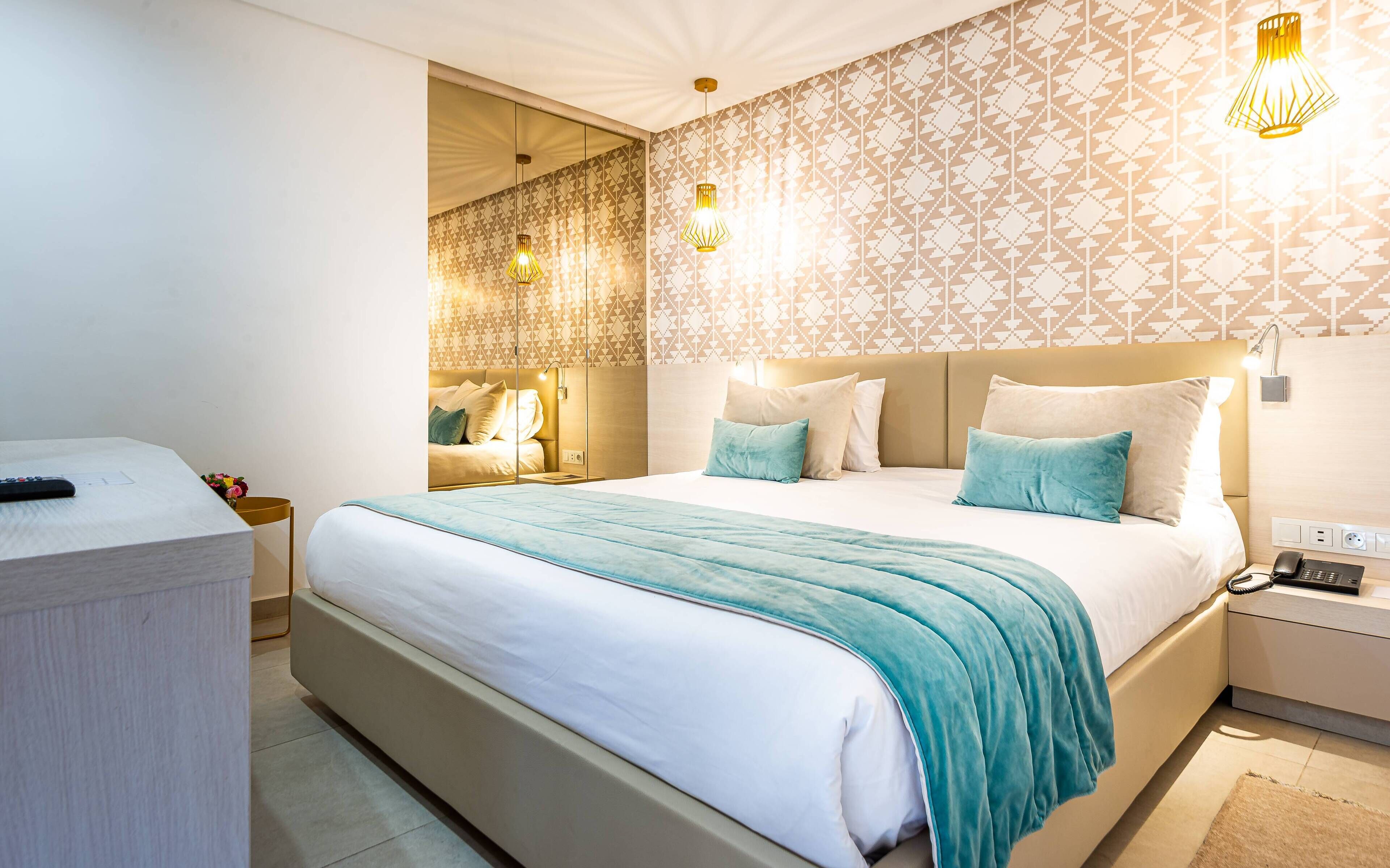 A modern hotel room with a large bed, bedside tables, and a desk with a phone.
