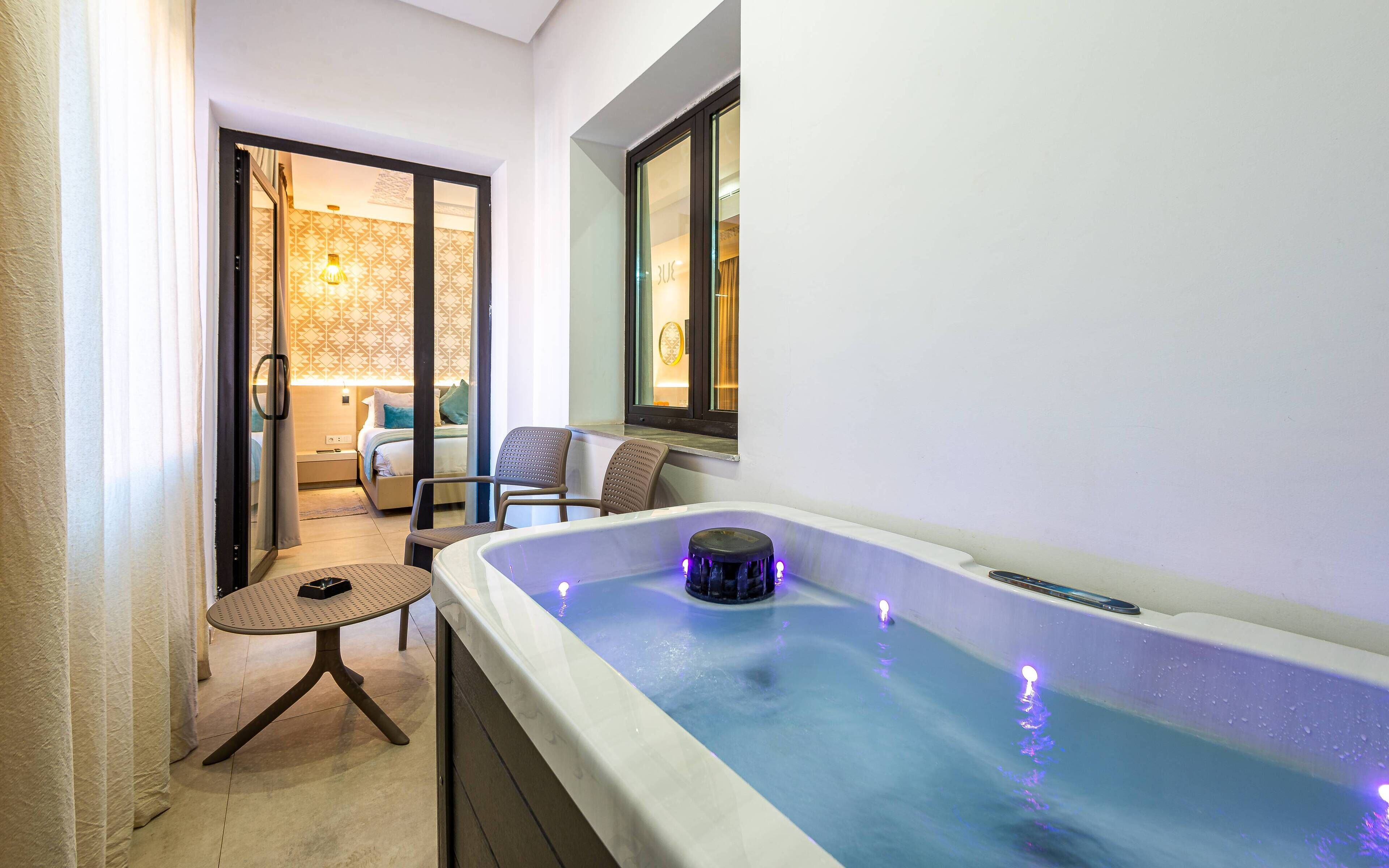 A spa area with a hot tub, a chair, and a bed with a patterned wall and a window.