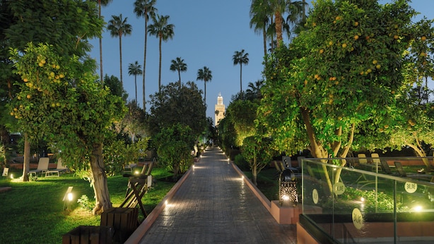 A pathway lined with palm trees and benches, leading to a distant tower. - TUI BLUE Medina Gardens – Adults Only – All Inclusive (Marrakech)