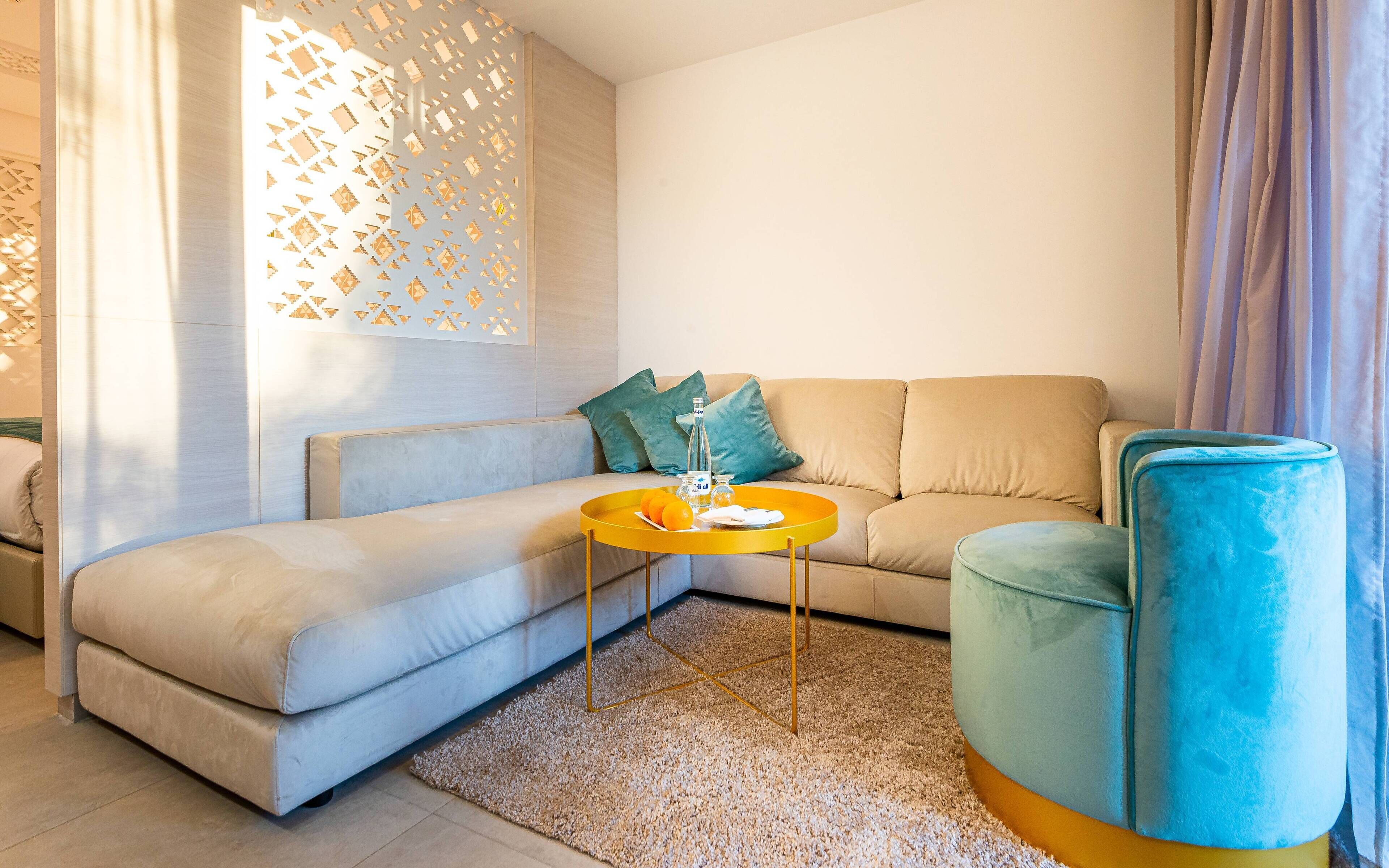 A modern living room with a beige sofa, a blue armchair, and a yellow coffee table.