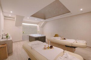 Una moderna stanza spa con lettino da massaggio, vasca da bagno e un mobile toilette con lavabo e specchio.