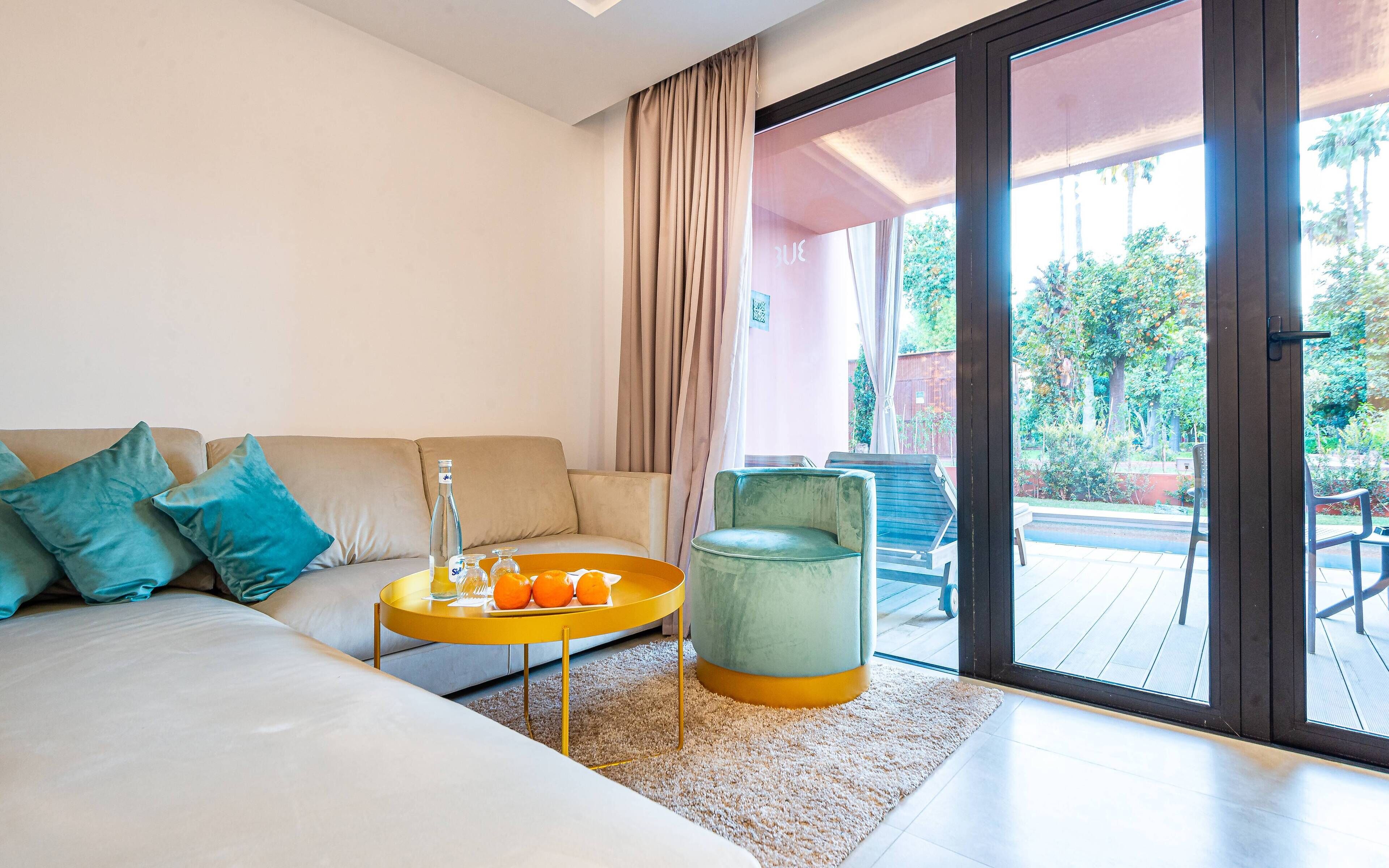 Una sala de estar moderna con un sofá, una mesa de centro con frutas y vistas a un balcón con mobiliario exterior.