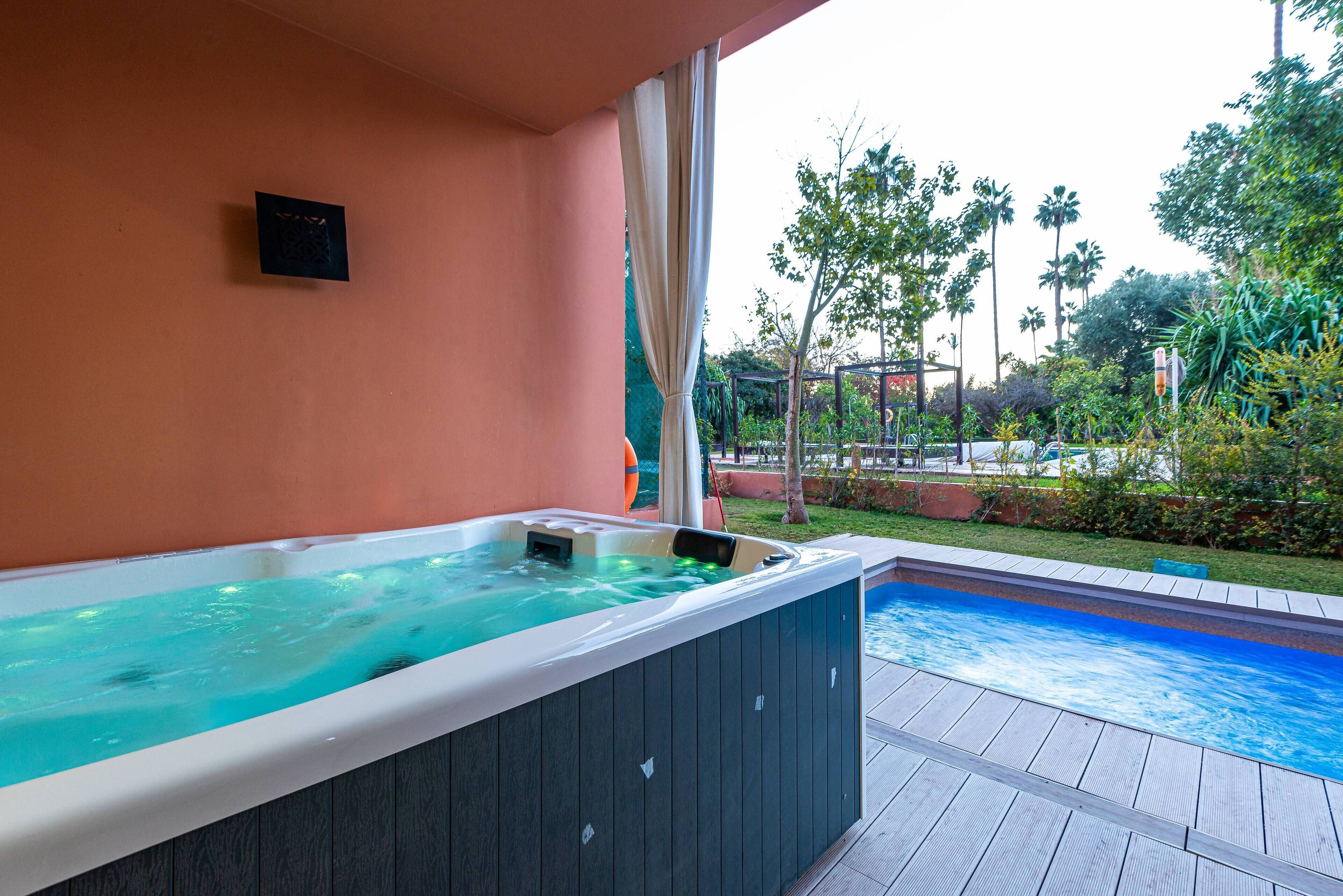 Una vasca idromassaggio con un pontile in legno e vista su una piscina e vegetazione.