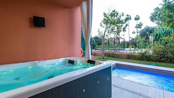 Una vasca idromassaggio con un pontile in legno e vista su una piscina e vegetazione.