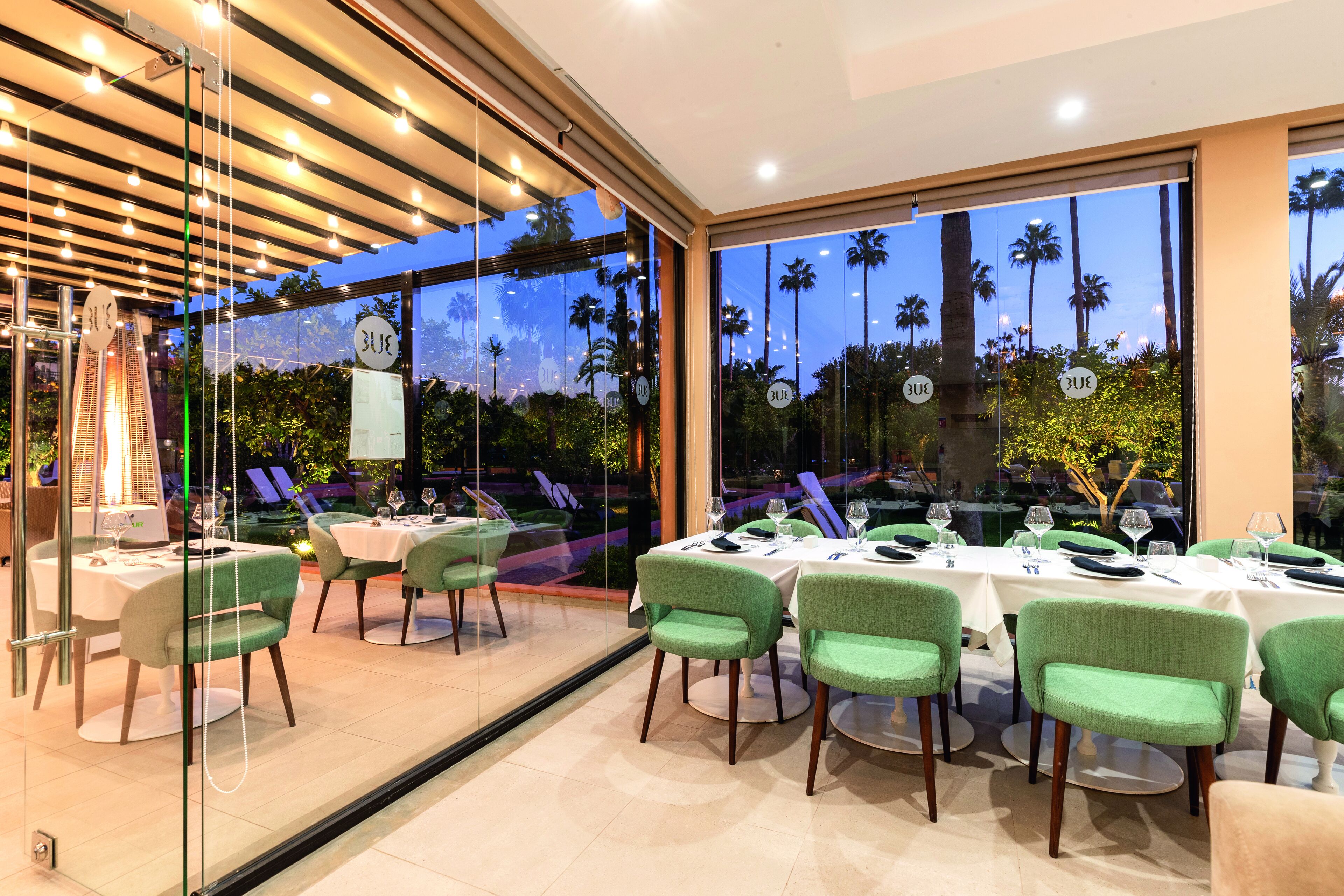 A restaurant with glass walls, green chairs, and tables set for dining.
