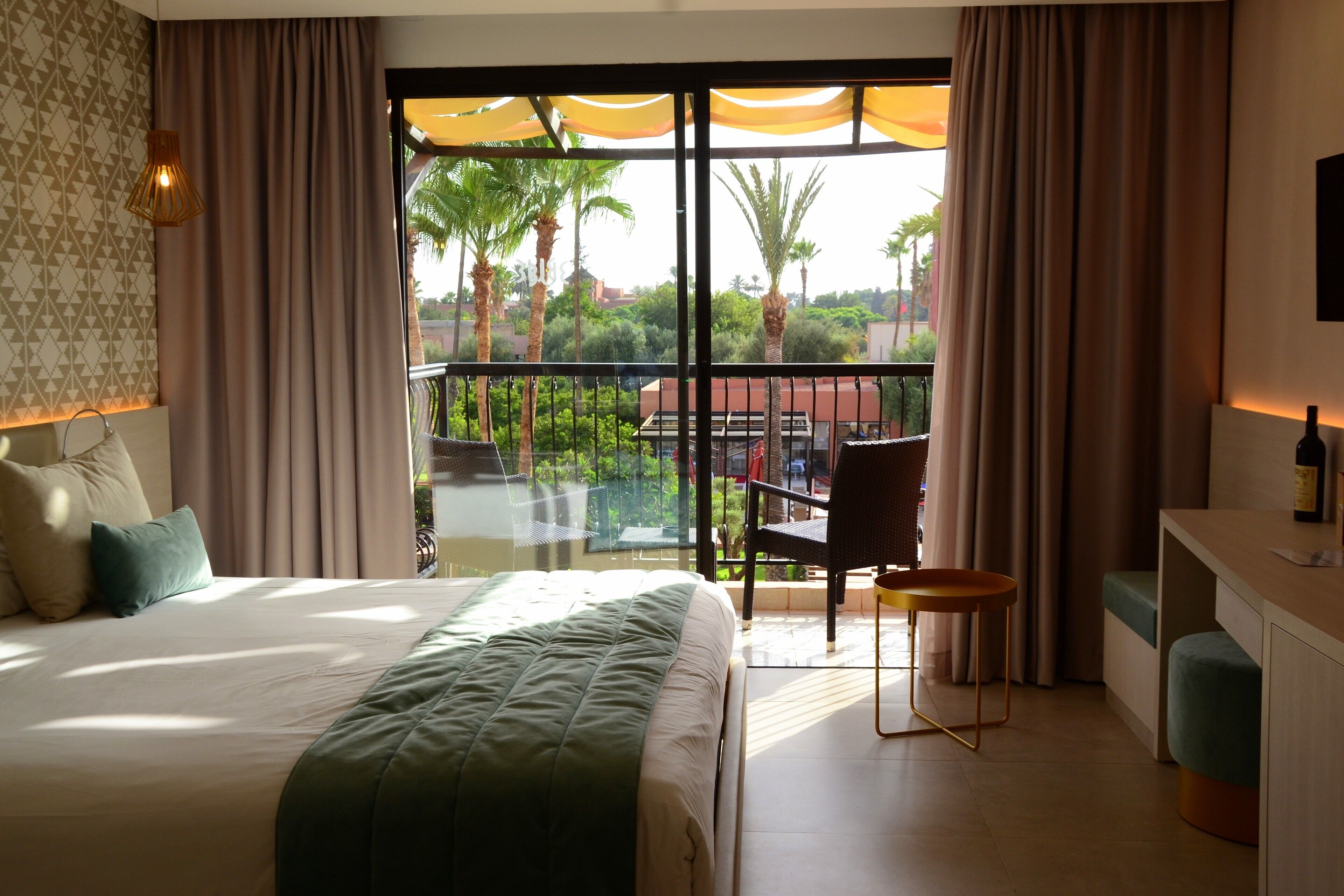 A hotel room with a balcony, a bed, a desk, and a chair.