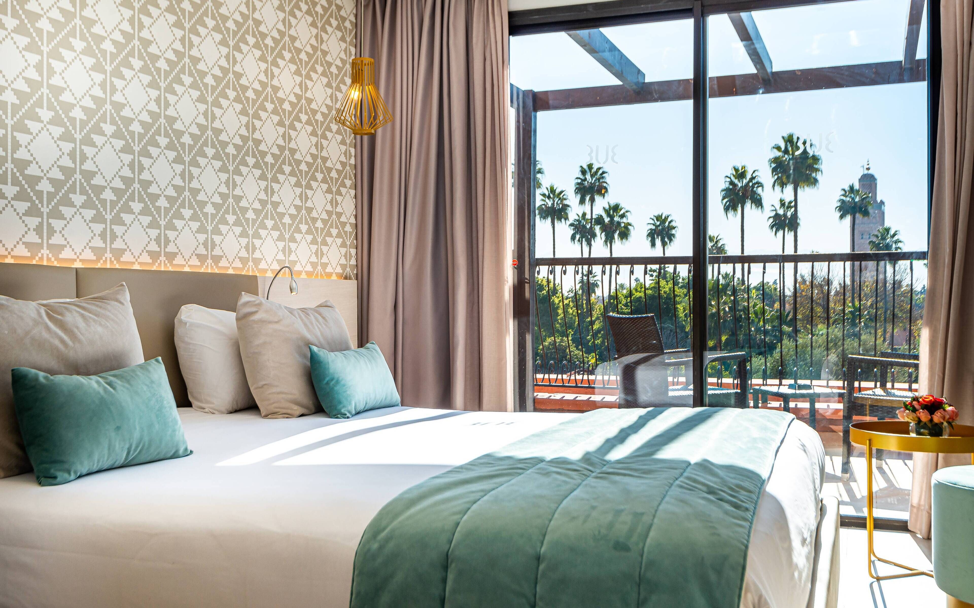 A hotel room with a large bed, a balcony with a view of palm trees, and a patterned wall.