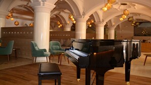 A grand piano in a spacious lobby with high ceilings and ornate columns, green upholstered chairs, and modern pendant lighting. - TUI BLUE Medina Gardens – Adults Only – All Inclusive (Marrakech)