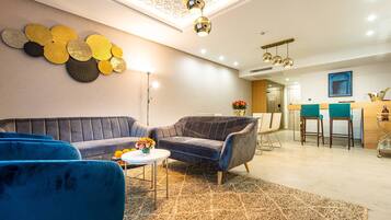 Un salon moderne avec un canapé, deux fauteuils, une table basse et un tapis. On aperçoit à l’arrière-plan un coin repas avec un bar et des chaises.