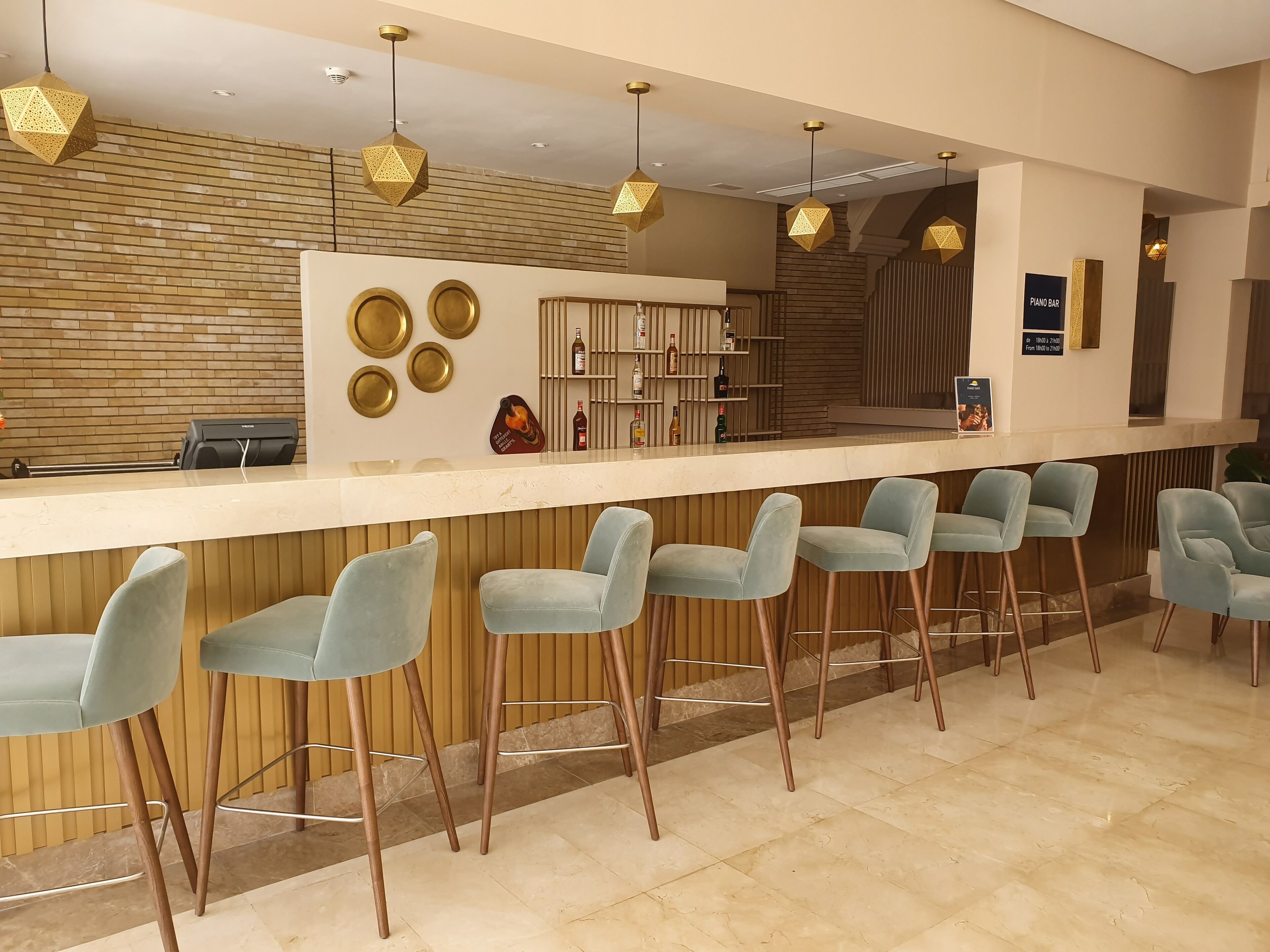 Una zona de bar con mostrador, taburetes y una variedad de botellas.