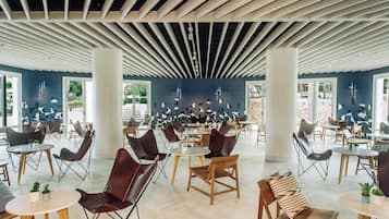Un vaste espace intérieur aménagé avec différents types de sièges, notamment des tables et des chaises, et de grandes fenêtres qui laissent entrer la lumière naturelle.