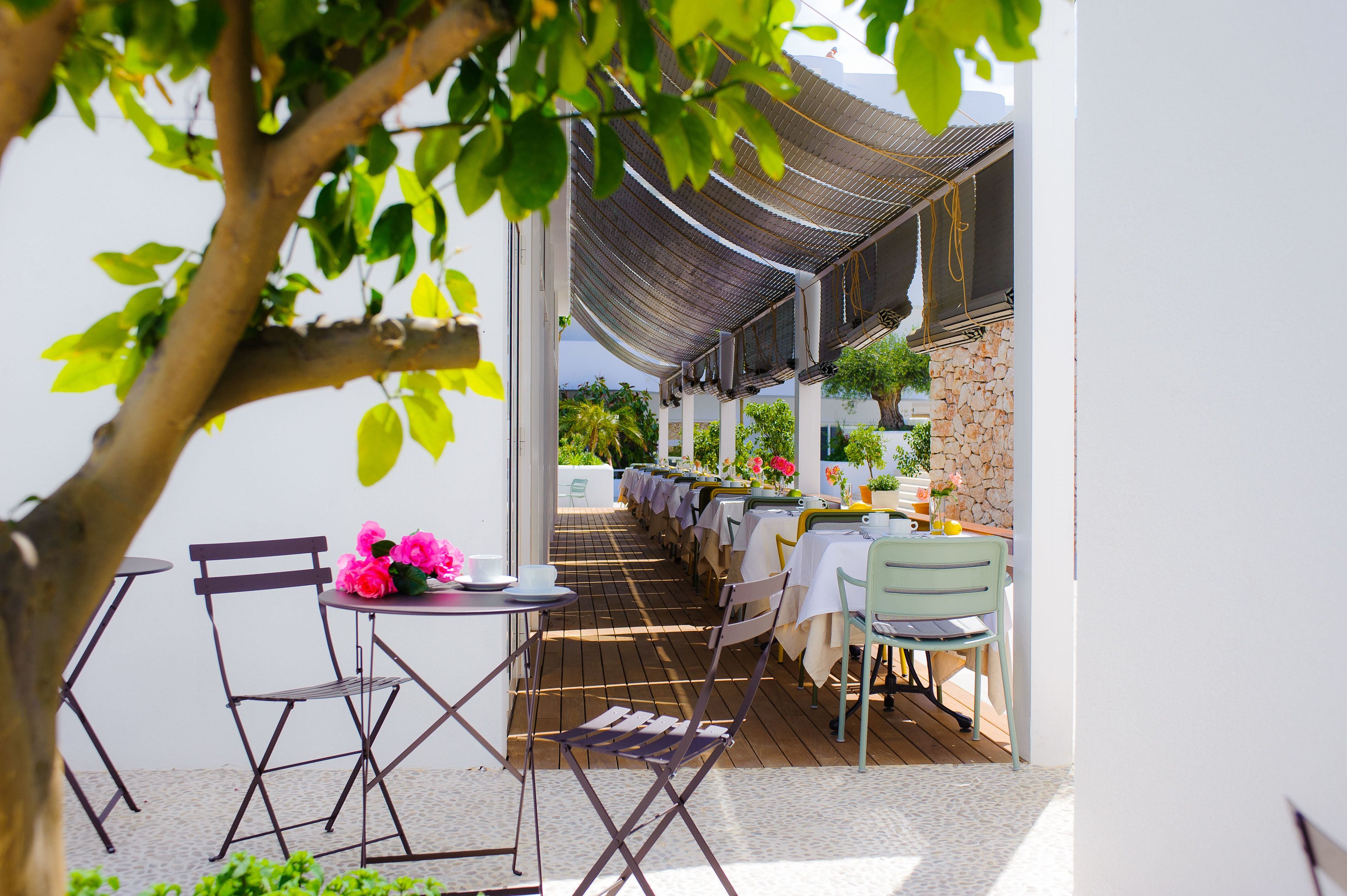 Un patio al aire libre con mesas, sillas, un árbol y un muro de piedra.