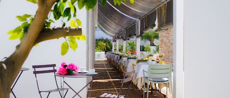 Une terrasse extérieure avec des tables et des chaises, un arbre et un mur en pierre.