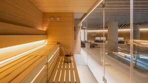 Ein moderner Wellnessbereich mit Holzliegen, einer Glastrennwand und einem Poolbereich.
